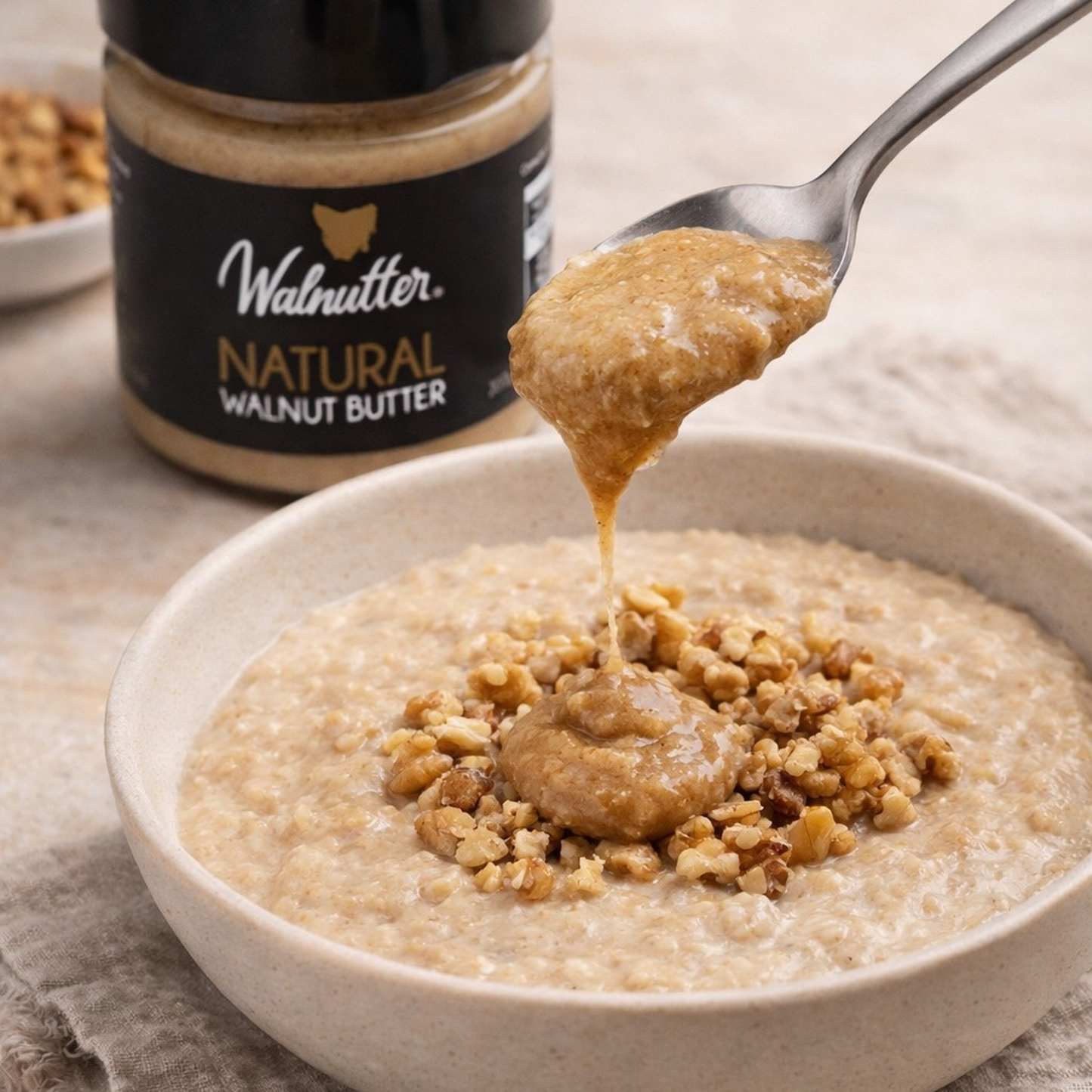Natural walnut butter being spooned over porridge with crushed walnuts in a breakfast bowl