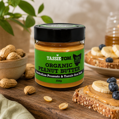 Jar of Tassie Tom organic peanut butter on a wooden surface with peanuts and toast.